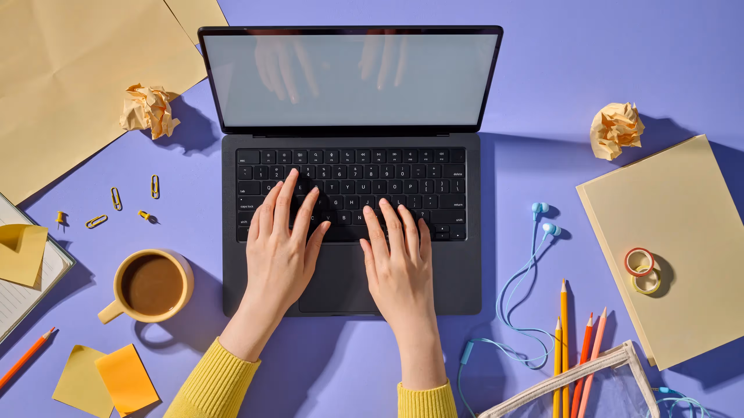 Hands on a laptop in a cluttered desk scene of bright colors.