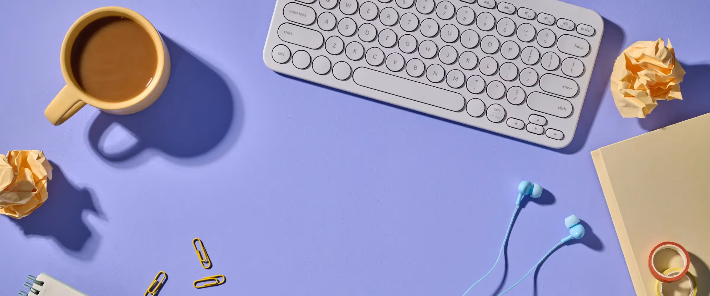 A keyboard, mug of coffee, earbuds and desk debris.