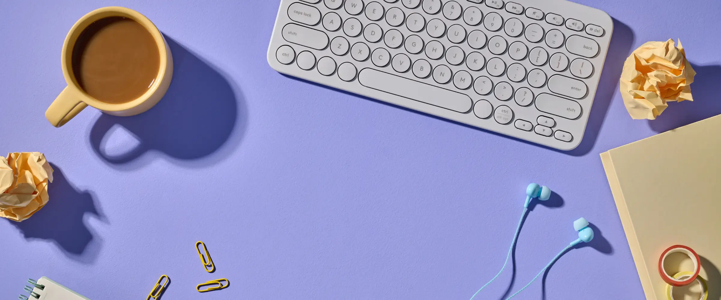 A keyboard, mug of coffee, earbuds and desk debris.