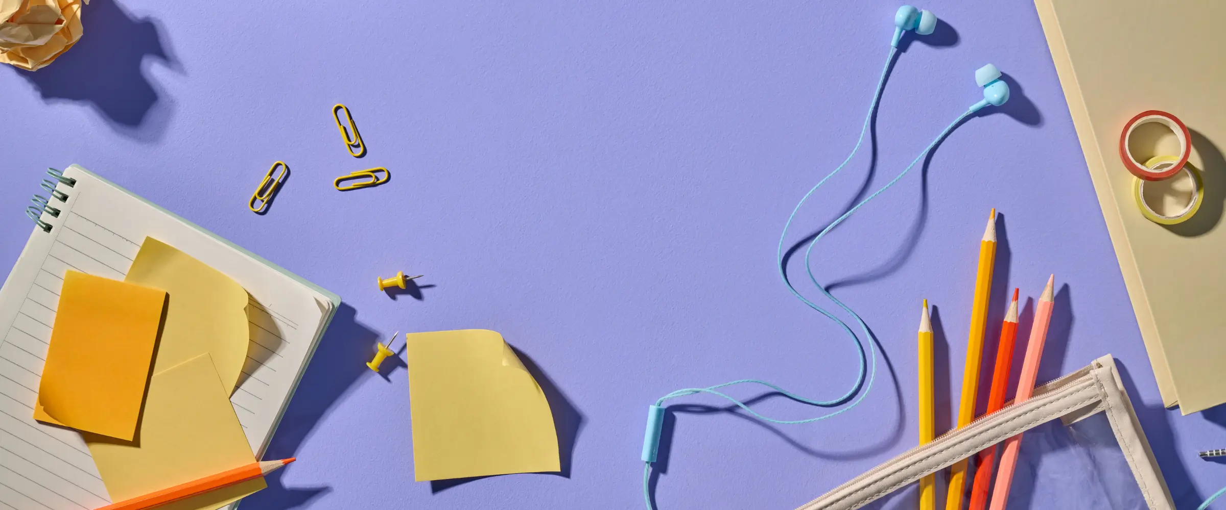 A desk surface cluttered with notes, stationery, pencils, and earbuds.