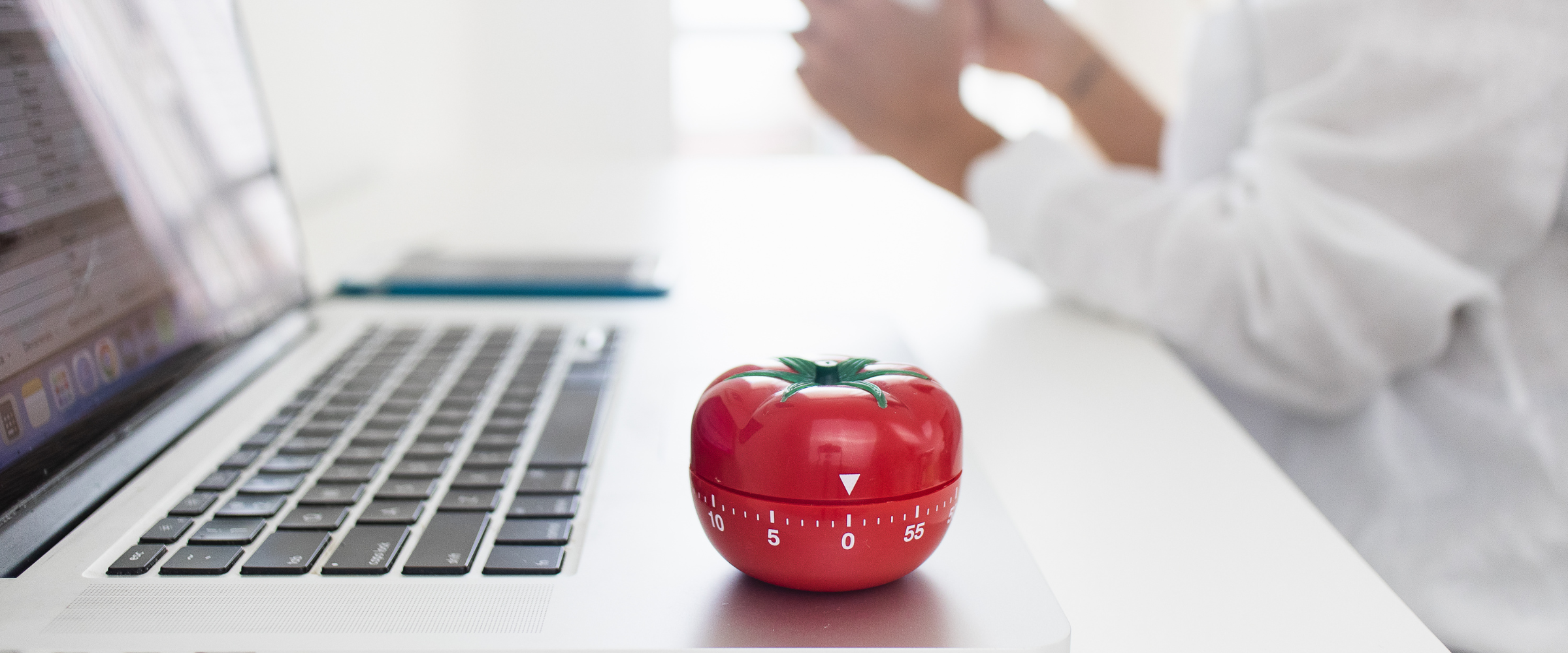 A tomato-shaped kitchen timer sitting on a laptop, portraying the Pomodoro technique.