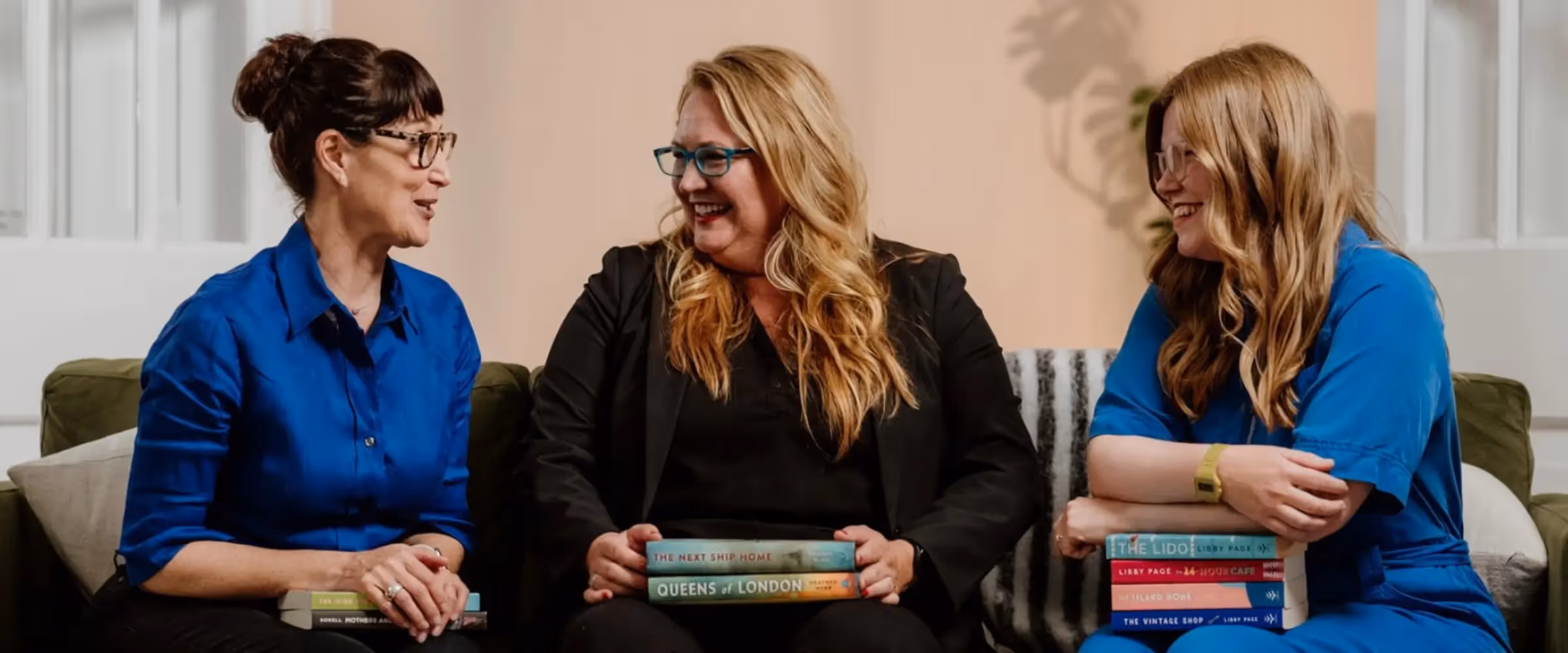 Three women engaged in conversation holding books.