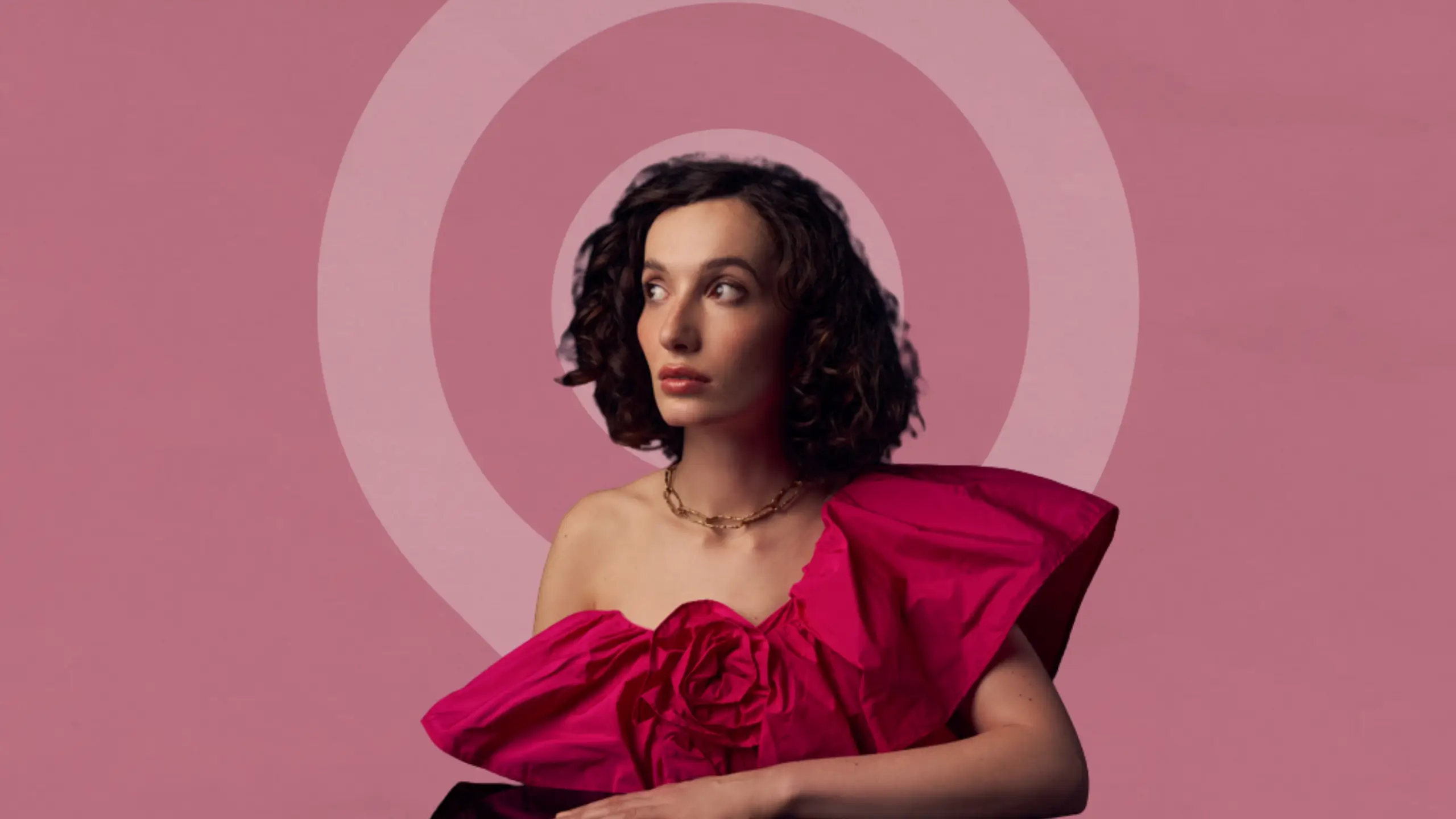 Portrait image of author and writing coach Bea Fitzgerald, wearing a vibrant pink dress, set against a dusky pink background.