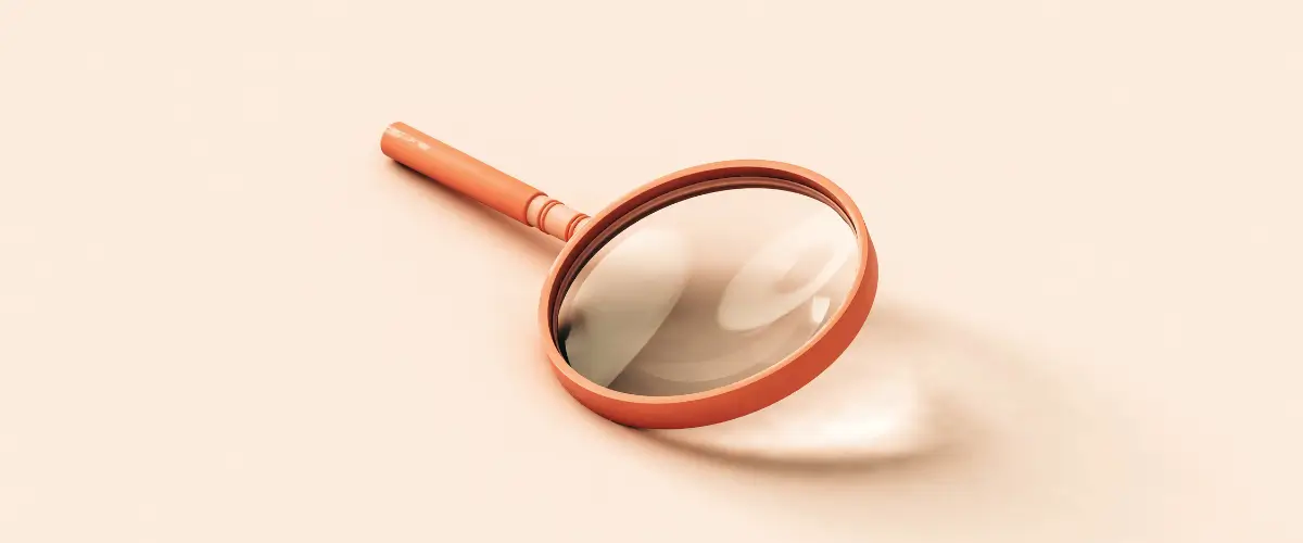 An orange magnifying glass lies on a peach-colored background.