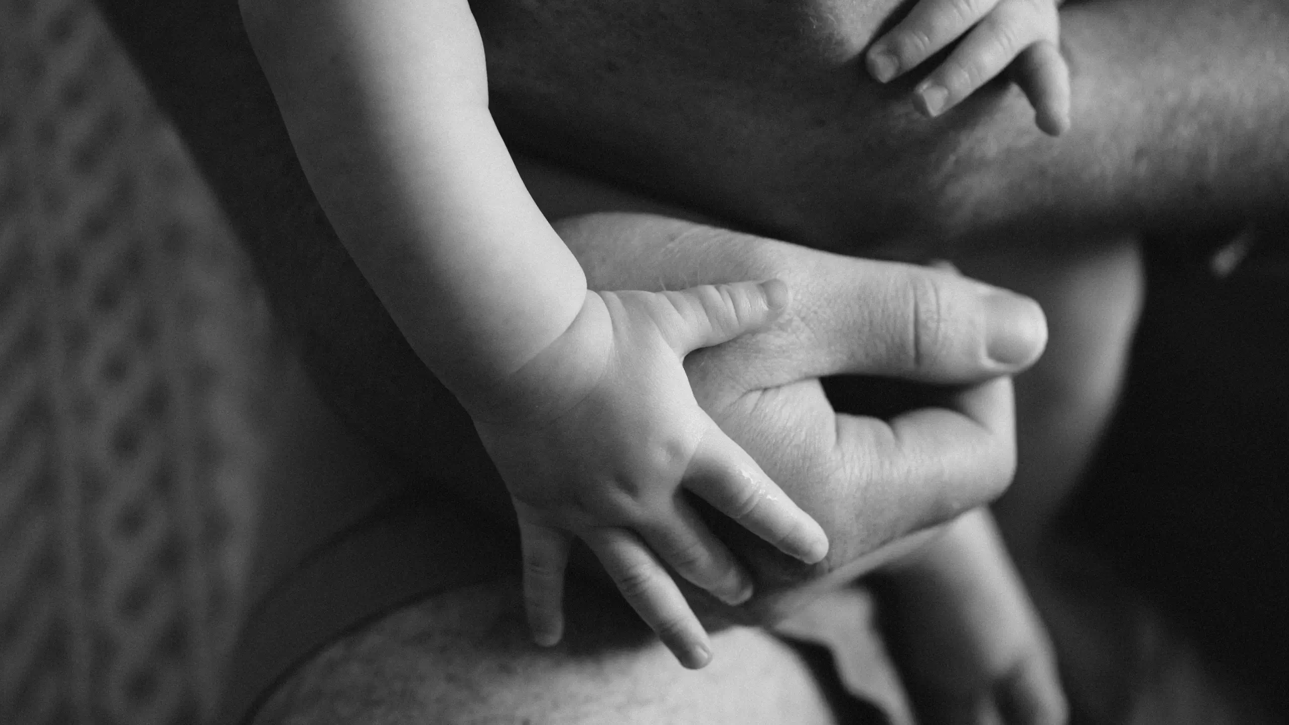 A baby's hands are seen holding a grown-up's arms.