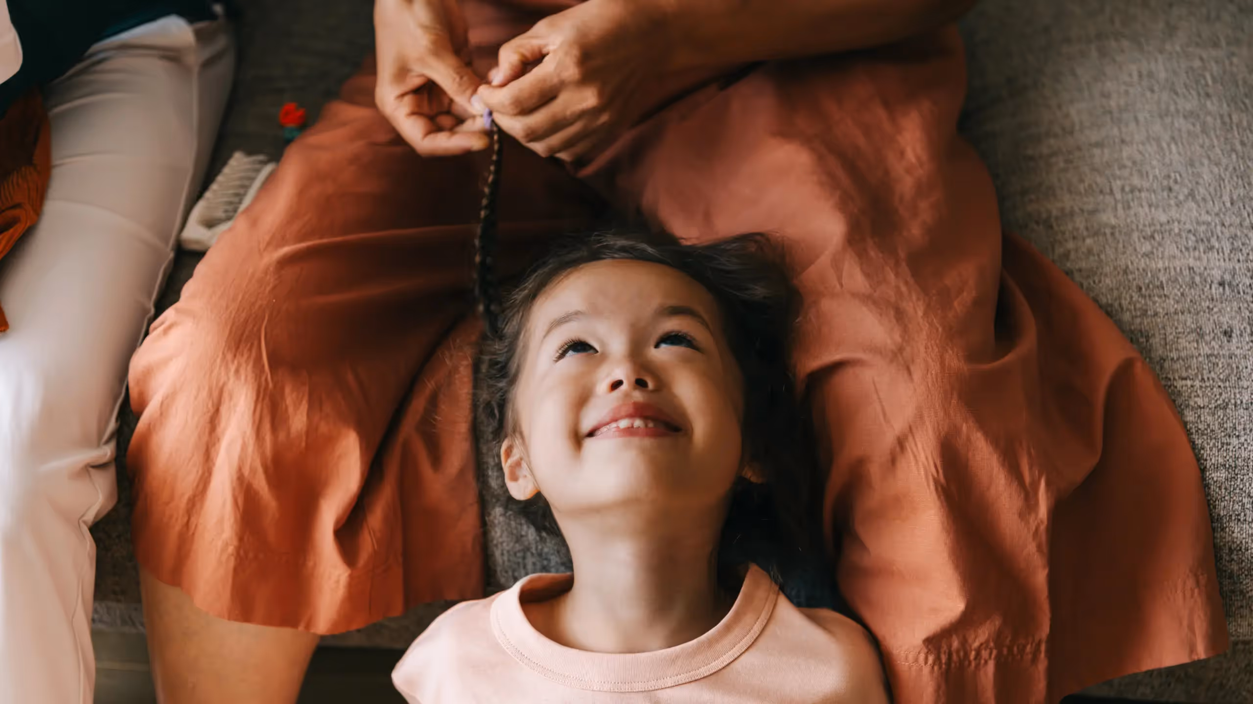 A child looks up smiling as someone plaits her hair.