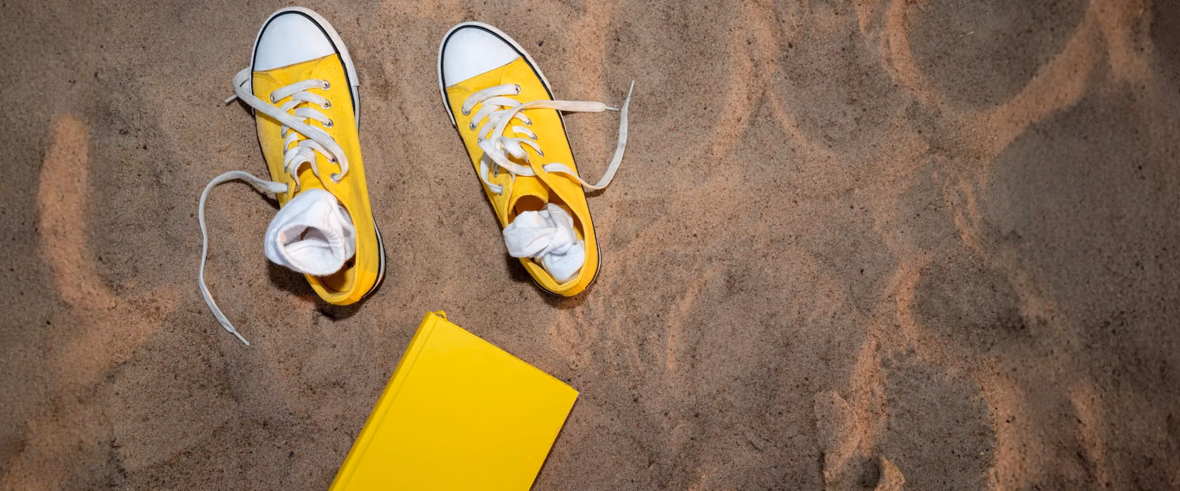 A pair of yellow shoes and a yellow book sit on a sandy beach.