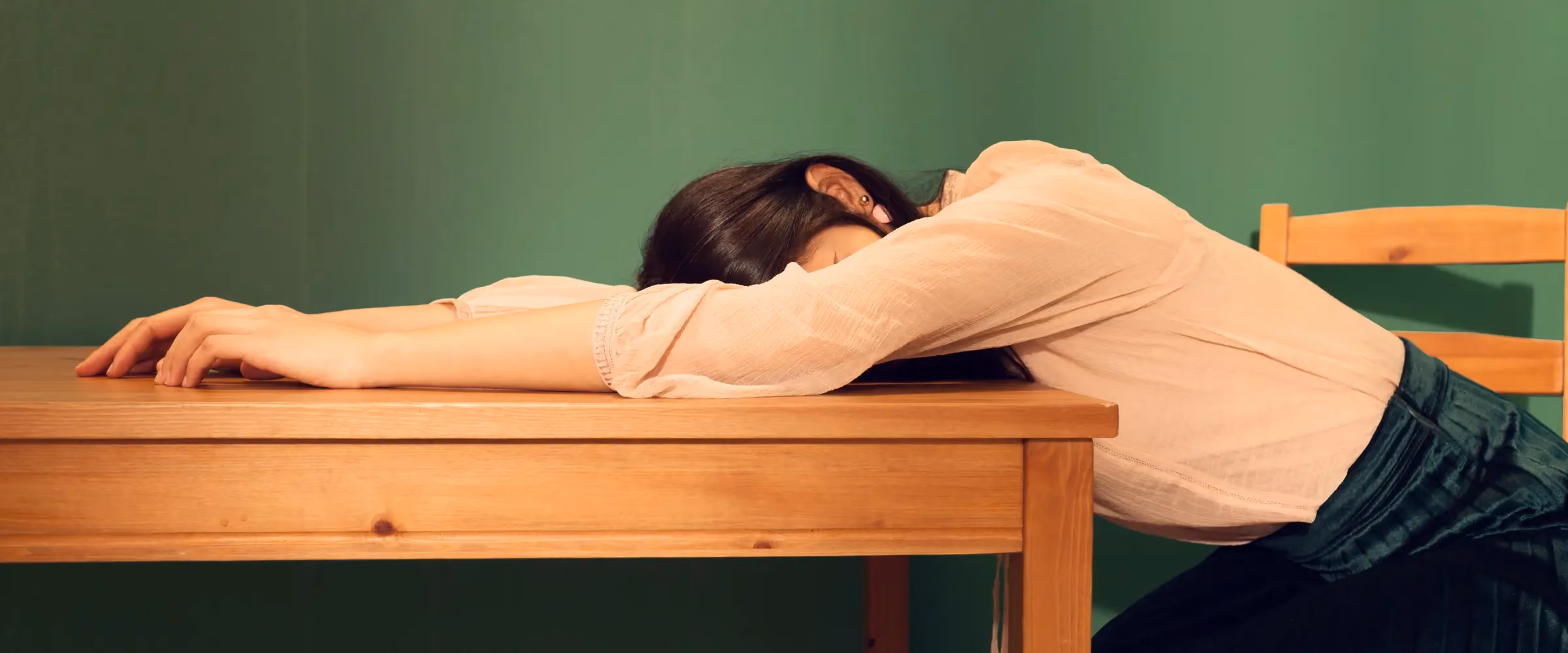 A woman collapses on her desk, her face obscured.