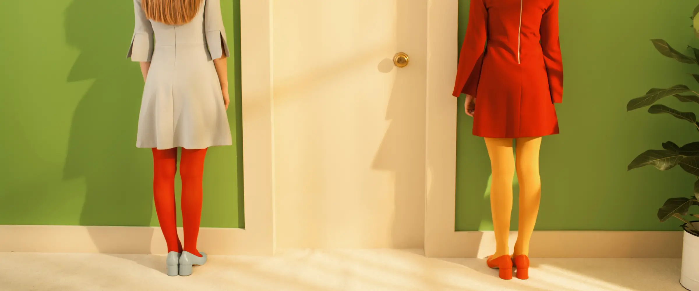 Two women in colorful outfits wait outside a door.