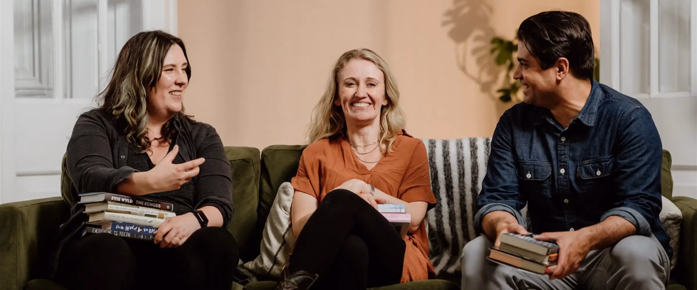 Three people sit on a sofa, holding books and smiling.