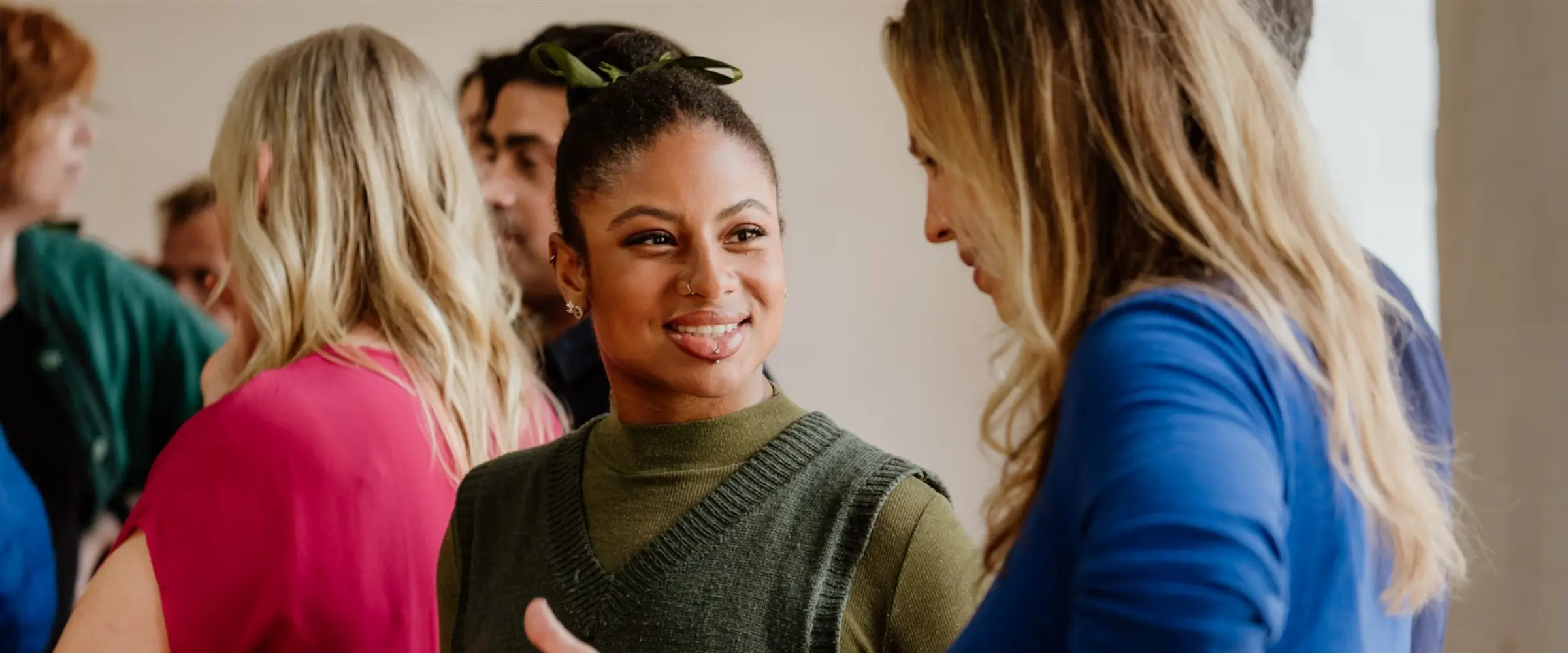 Two women in conversation in a room of other people, all dressed in colorful clothing.