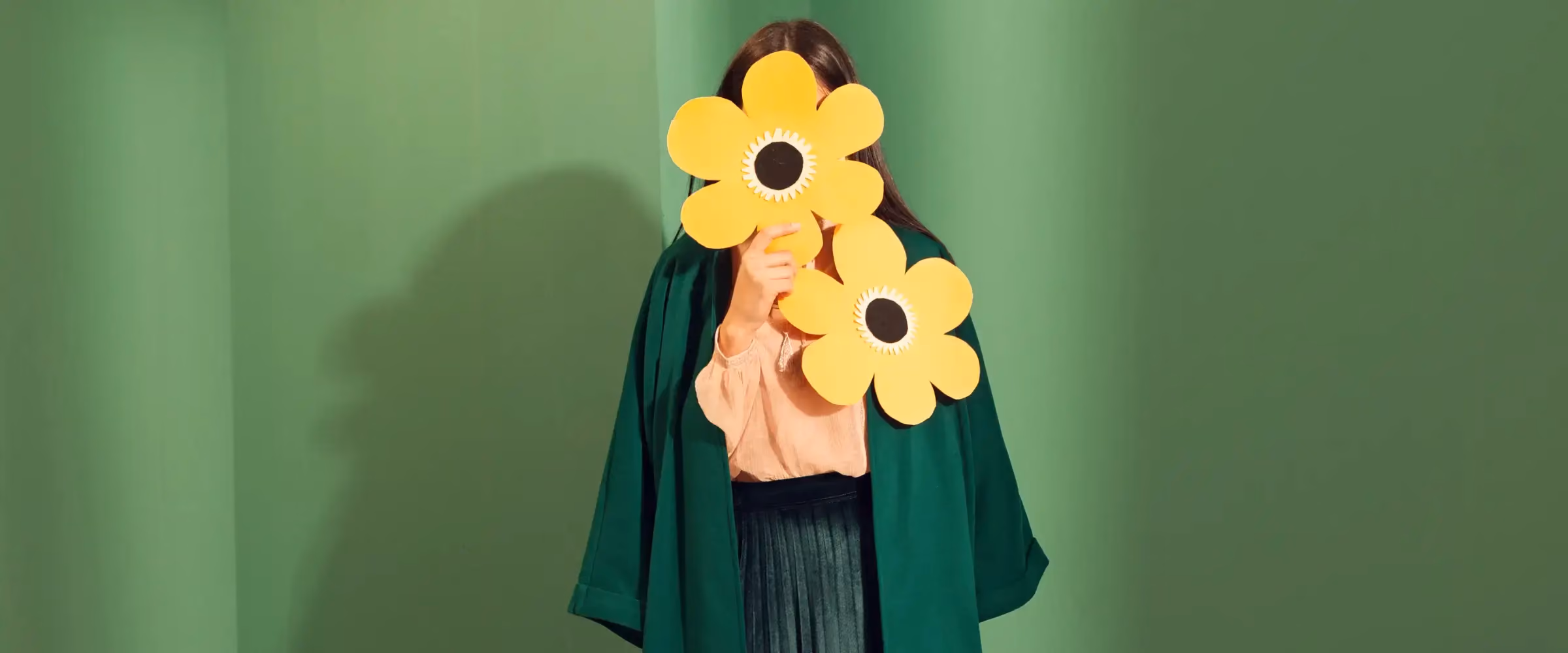 A woman holds a pair of oversized flowers that cover her face.