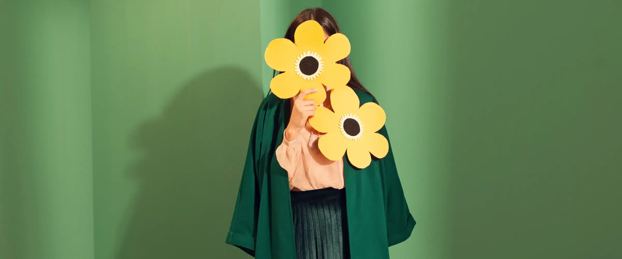 A woman holds a pair of oversized flowers that cover her face.