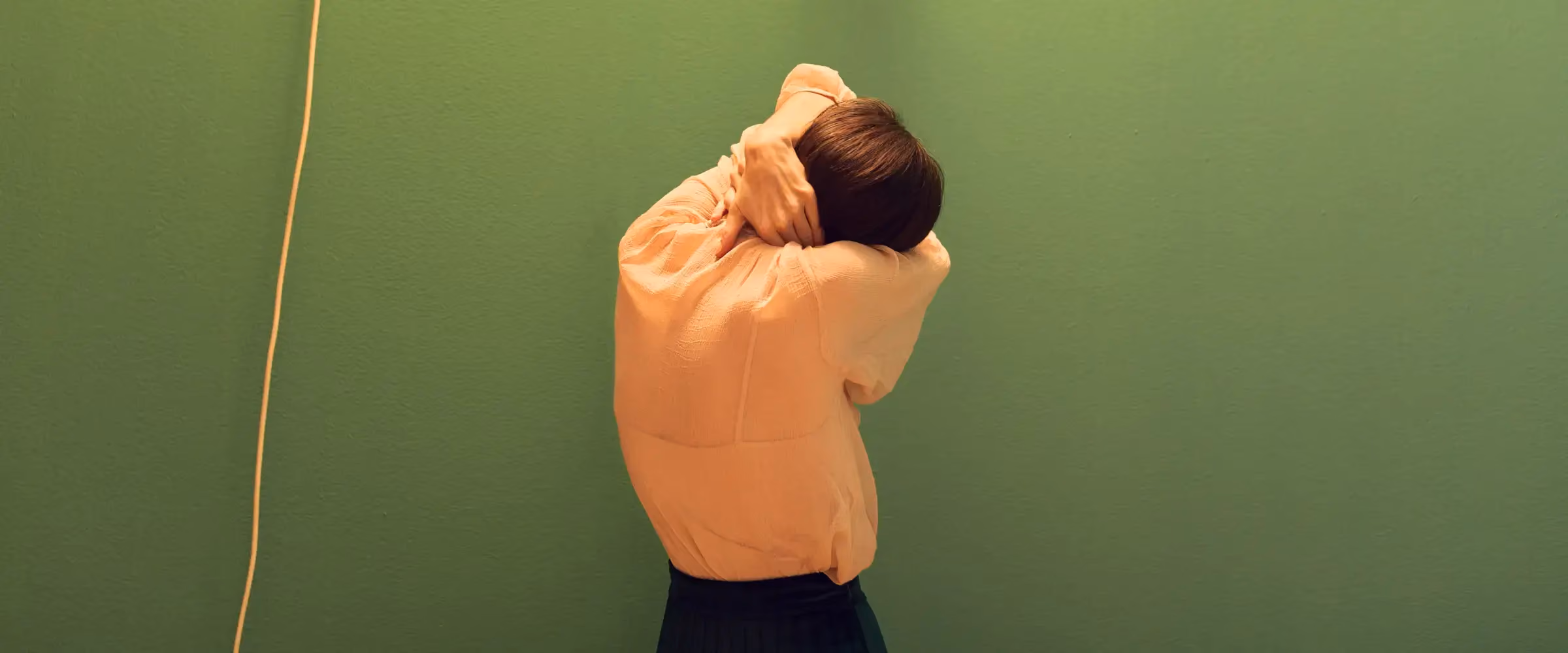 A woman has her back turned to the camera and holds her neck.