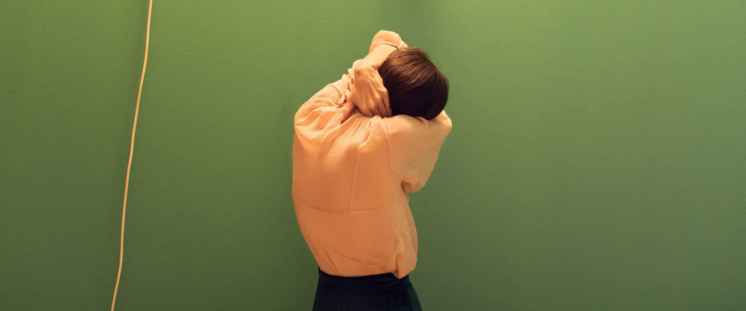 A woman has her back turned to the camera and holds her neck.