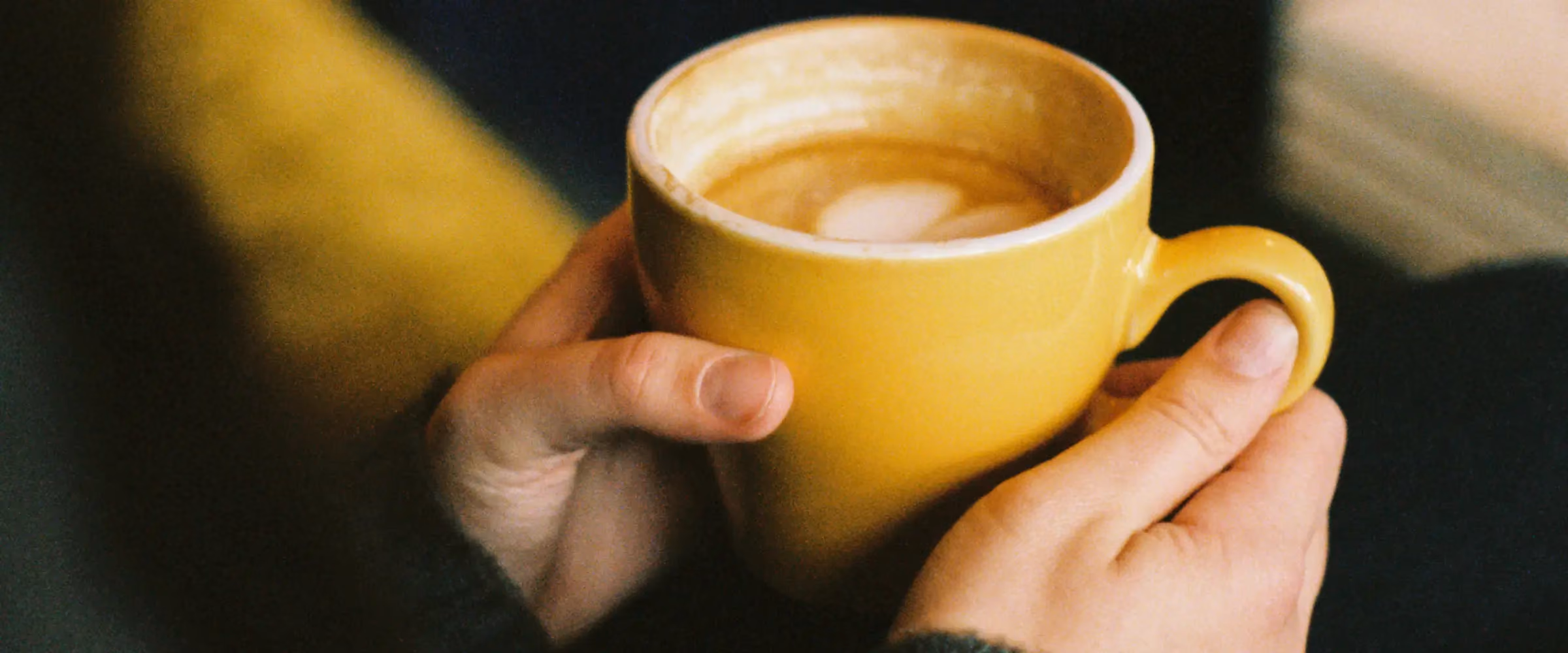 Hands holding a yellow cup of coffee.