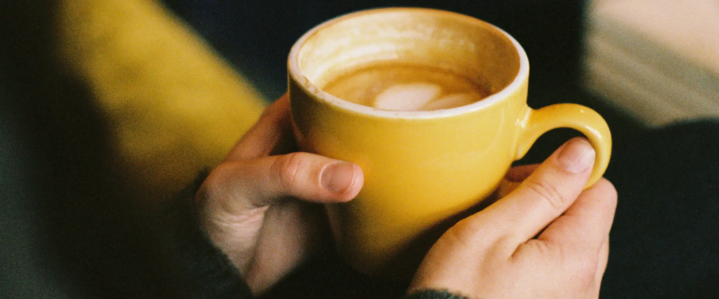 Hands holding a yellow cup of coffee.