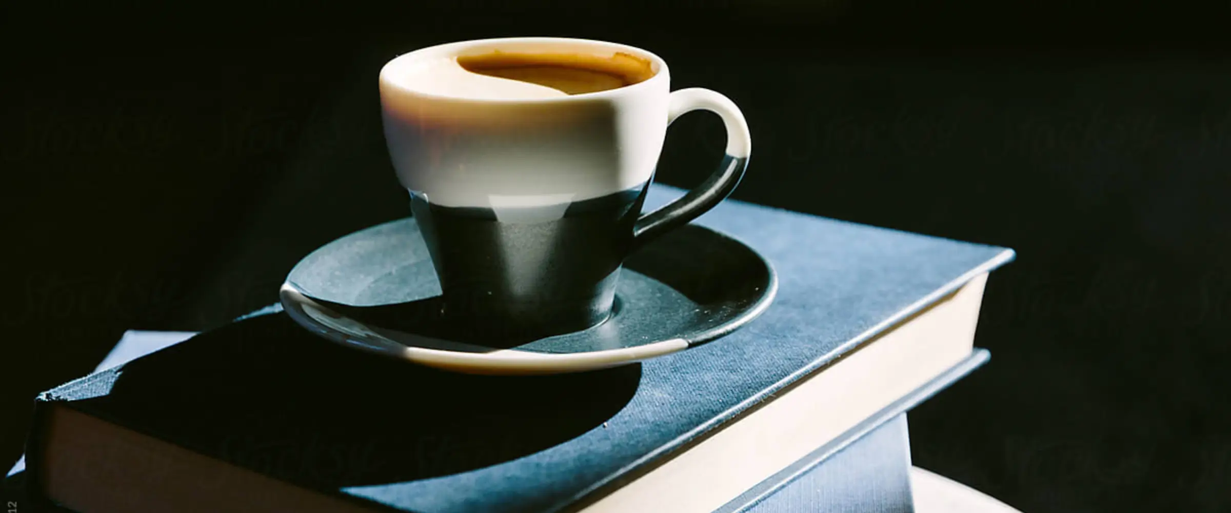 A cup of espresso sits on top of a pile of books.