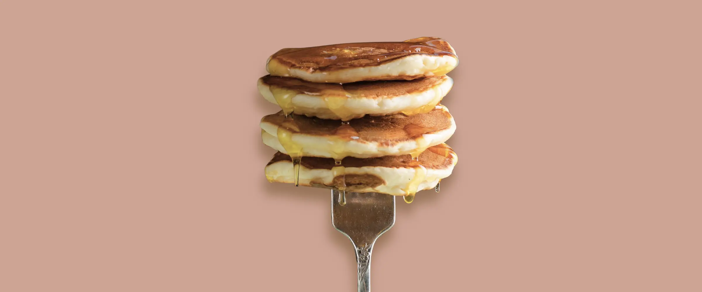 A stack of four pancakes, each dripping syrup, stacked on the tines of a fork.