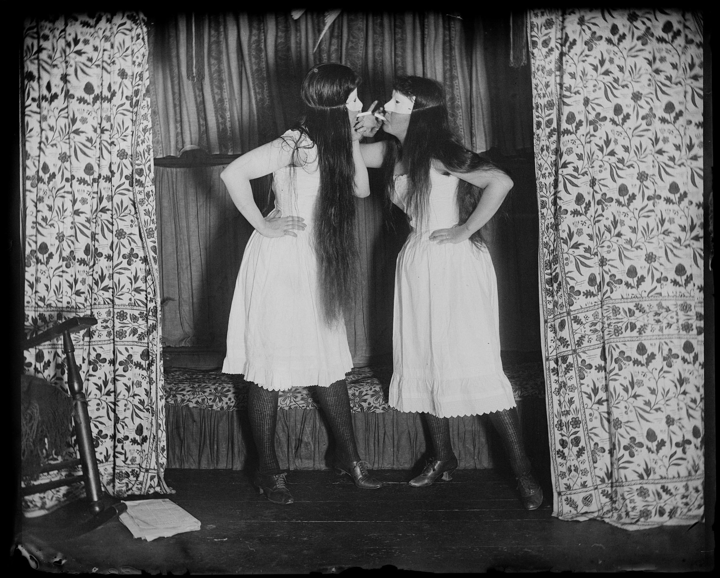 1891, Alice Austen and her friend Trude pose in sleeveless undergarments and short skirts, hair down, smoking near St. John's Episcopal Church.