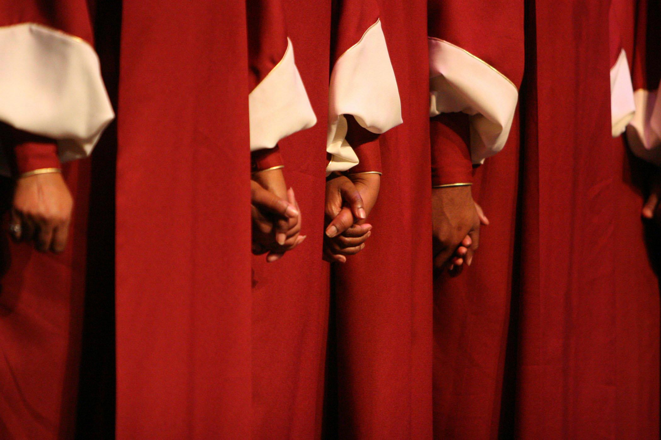 A row of people in red robes hold hands.