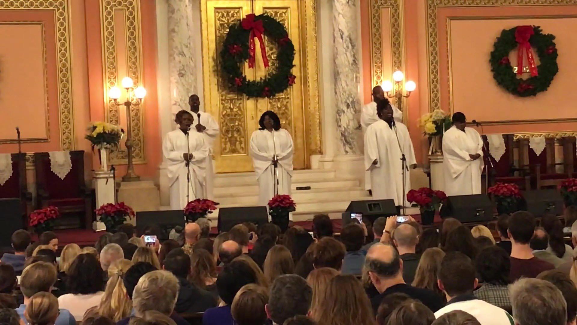 A crowd is seated, watching the Gospel ceremony performed by performers in white robes.