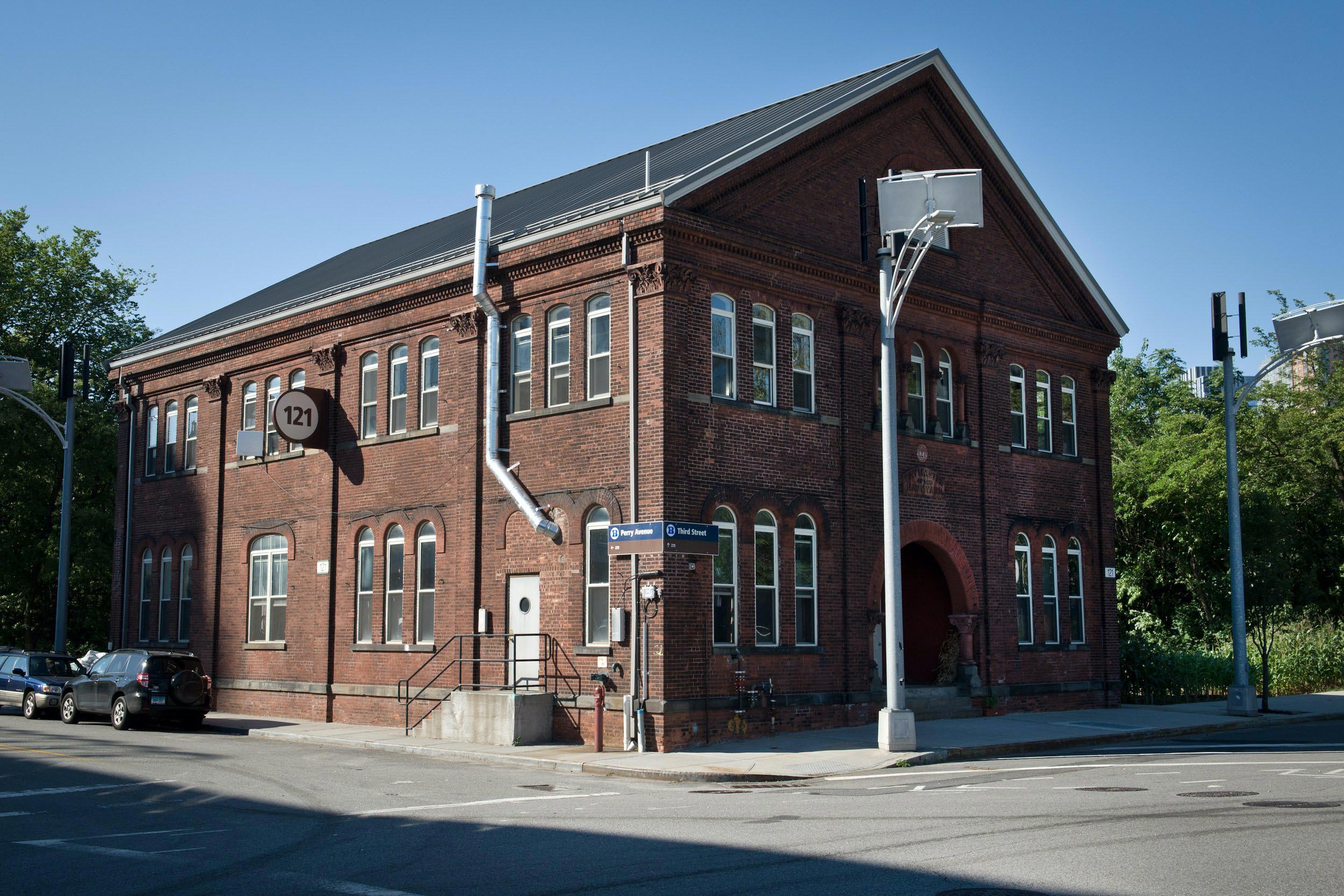 Exterior of the distillery, a large brick building with many arched windows.