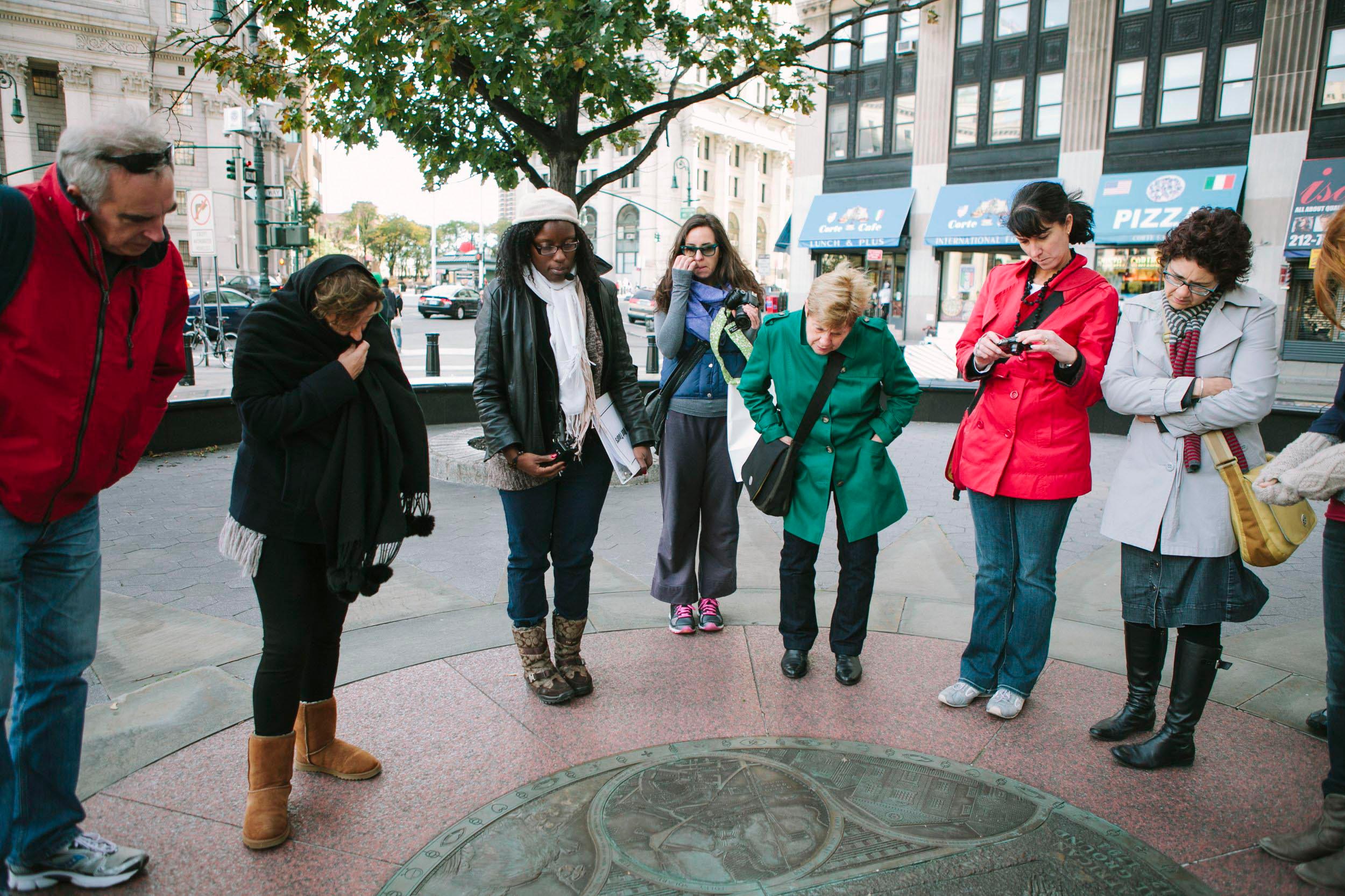A group of people analyze a copper monument built into the ground.