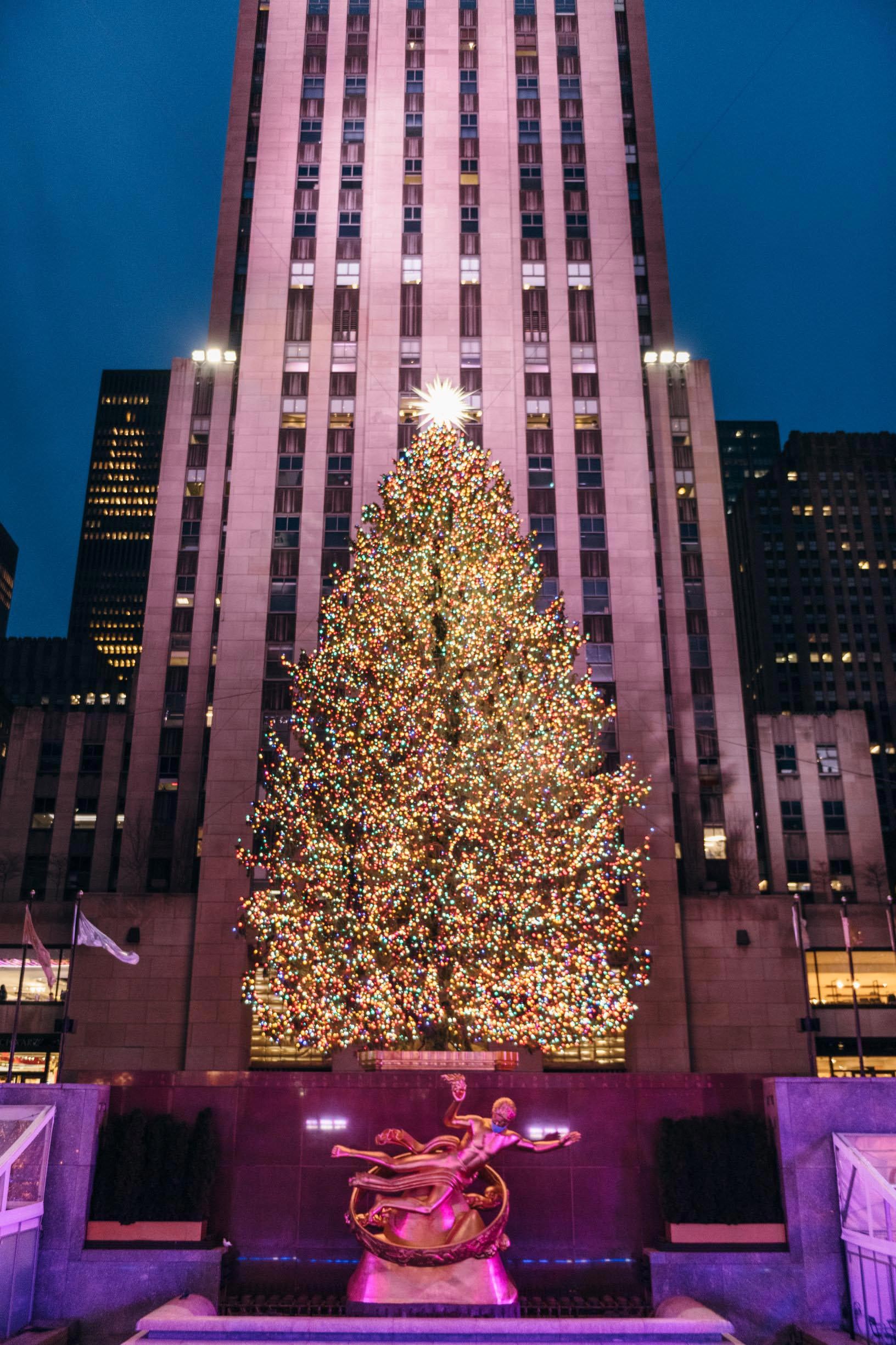 A Christmas tree covered in colorful lights and topped with a dazzling star sits in front of Rockefeller Center.