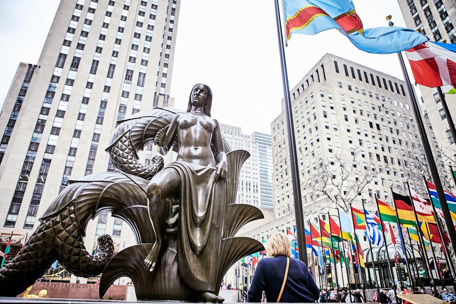 A bronze statue of a mermaid, surrounded by flags.