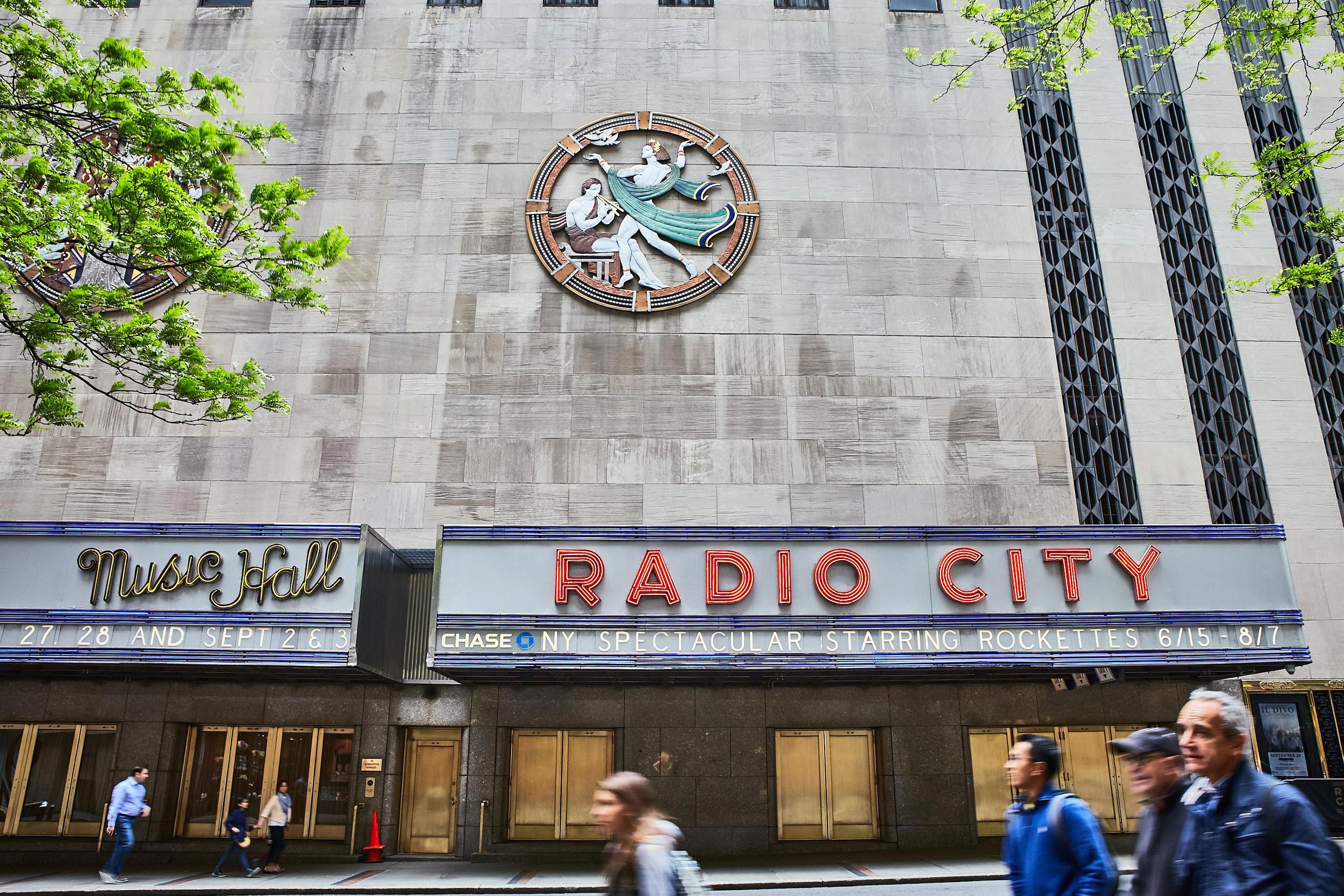 "Music Hall" and "Radio City" signs hang below an art deco piece representing song.