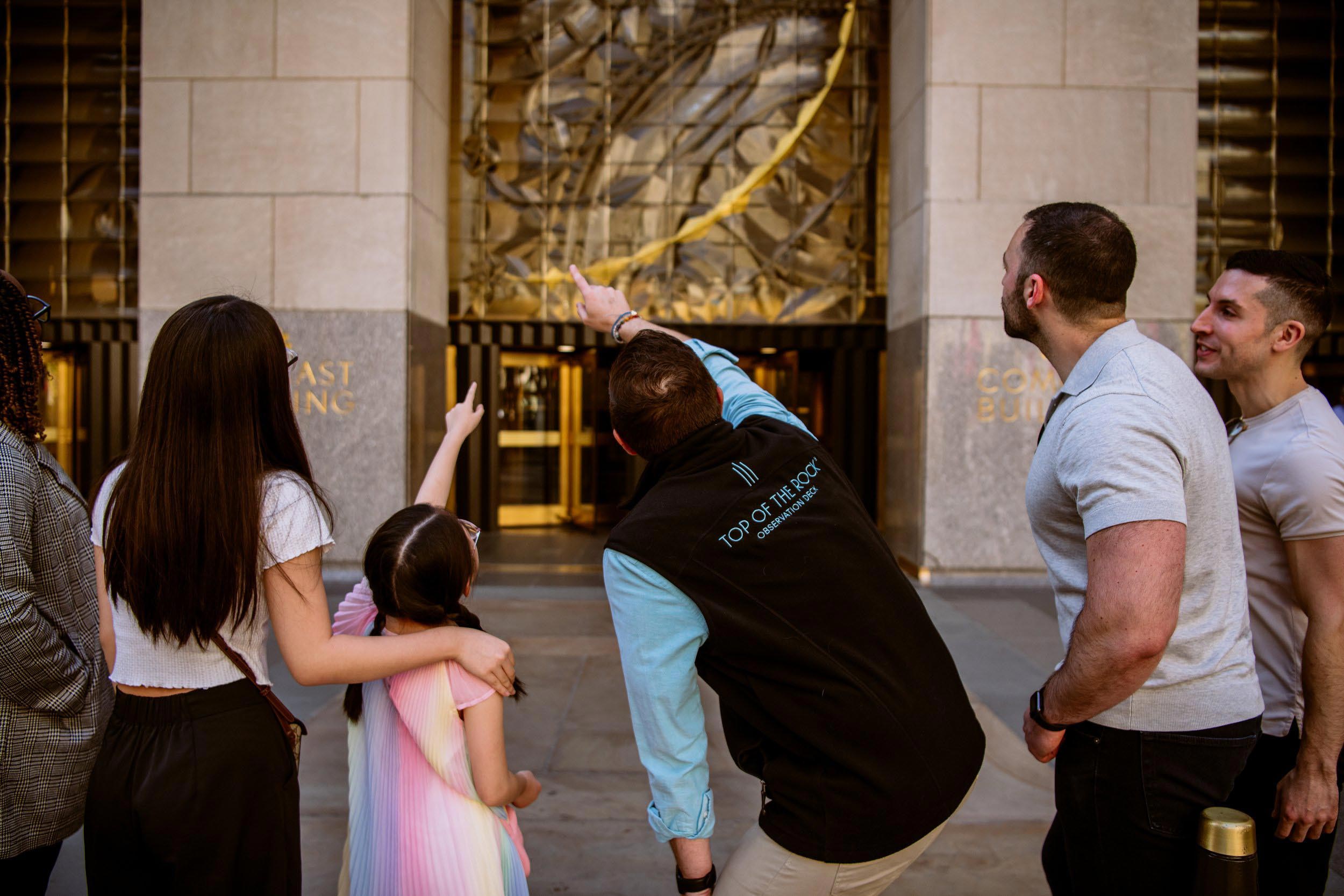 A small crowd gazes and points above the entrance to a large stone building.