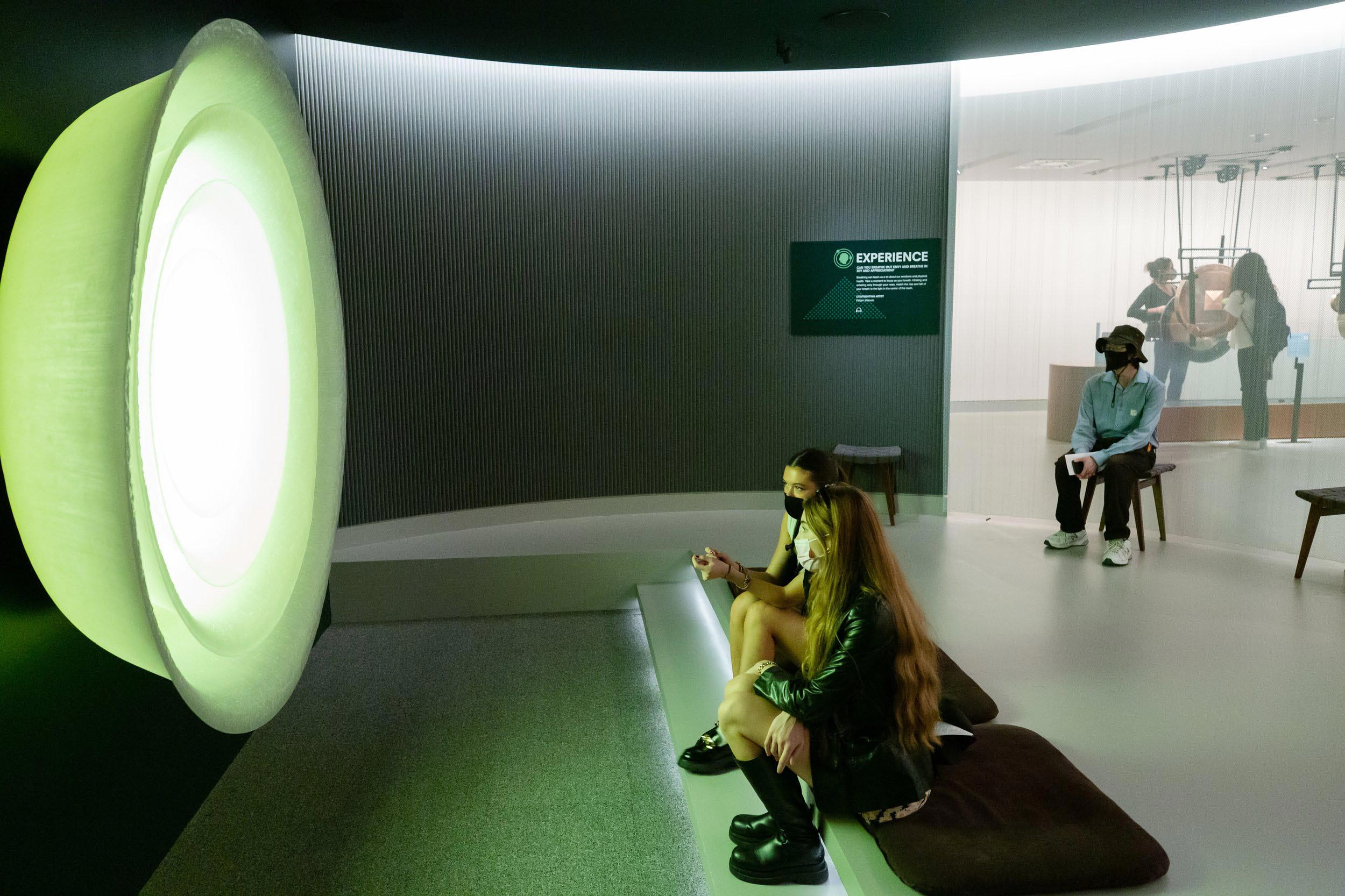 Two museum visitors sit in the bright light of the interactive Mandala Lab exhibit.