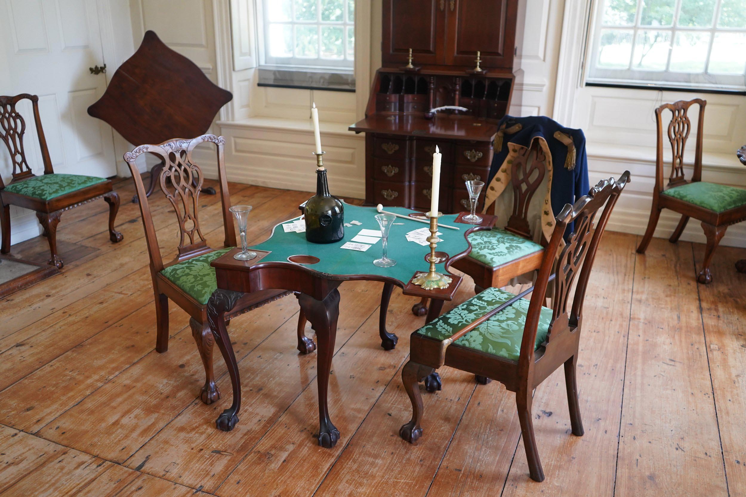 An intricate card table surrounded by green upholstered chairs.