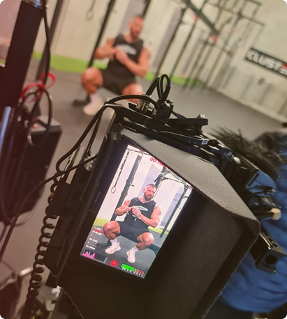 Camera screen showing a man in athletic wear squatting in a gym, with him blurred in the background.