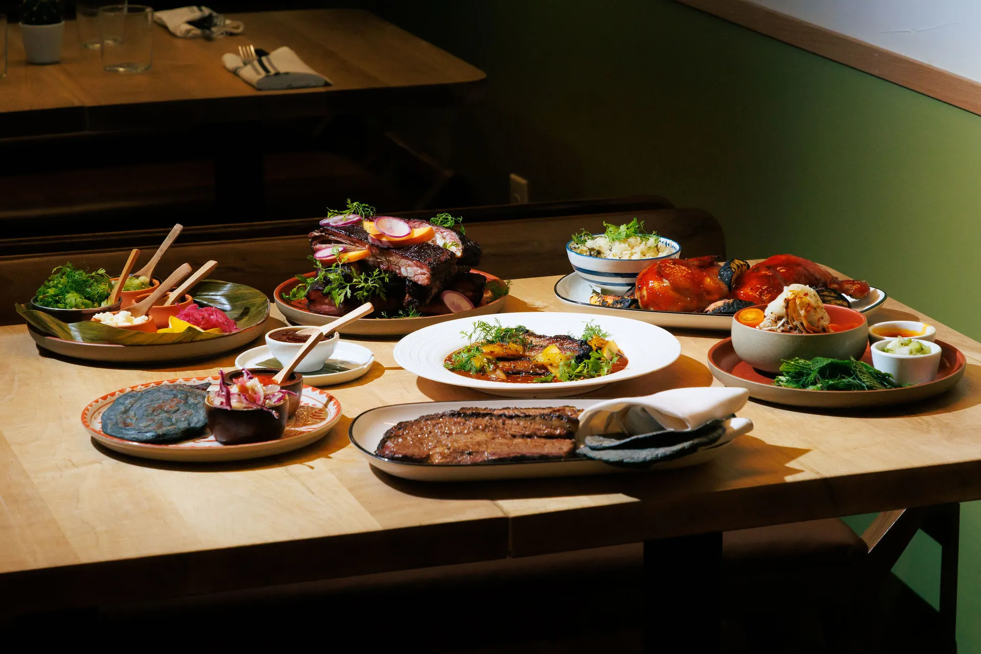 Family-style spread of fire-cooked dishes from the 2fifty BBQ x Amparo Fondita residency, featuring brisket, blue corn pupusas, mole pork belly, and chamoy ribs. Photo by Sophie Mac.