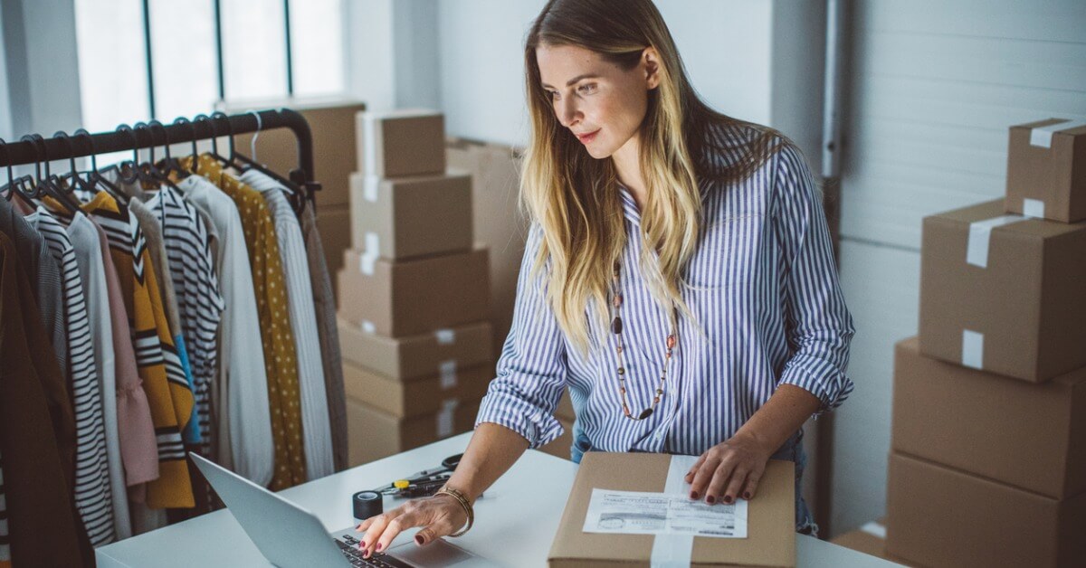 femme dans un entrepot avec des vêtements et des cartons préparant une commande