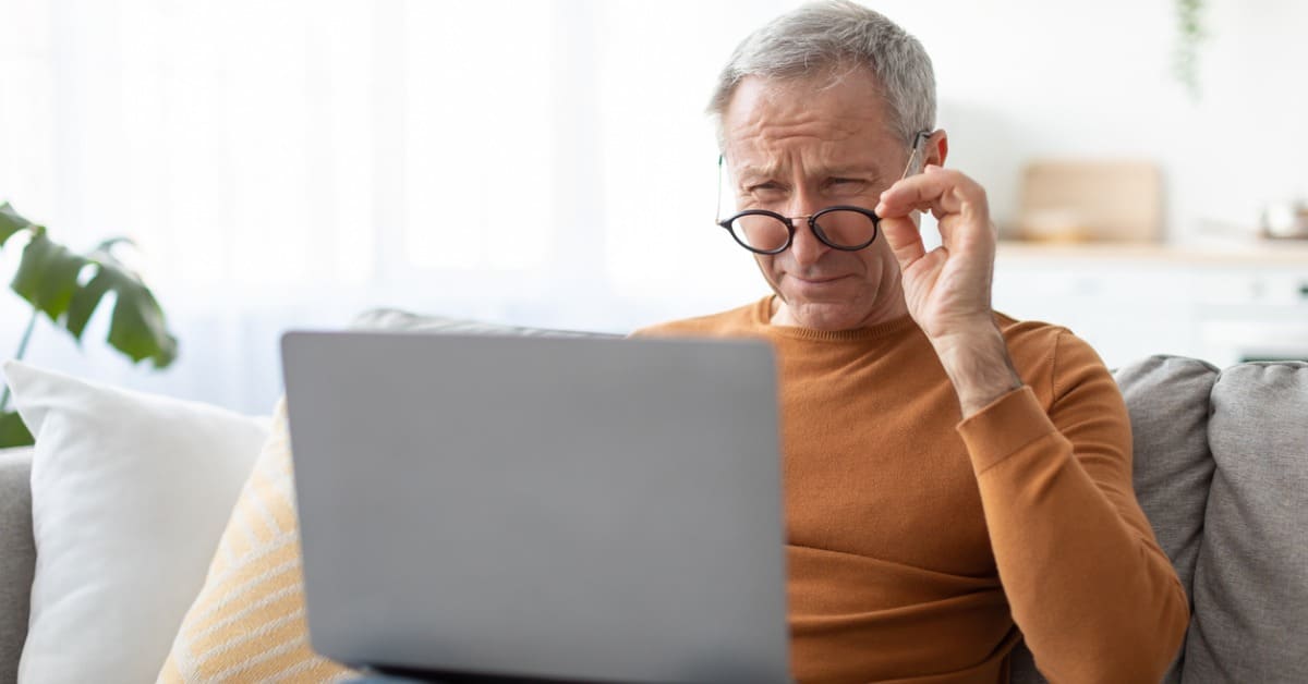 Elderly person adjusts their glasses in front of a computer screen