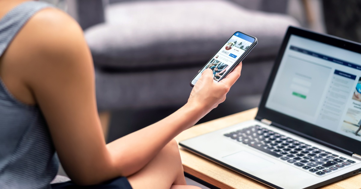 femme de dos tenant un téléphone et regardant un ordinateur 
