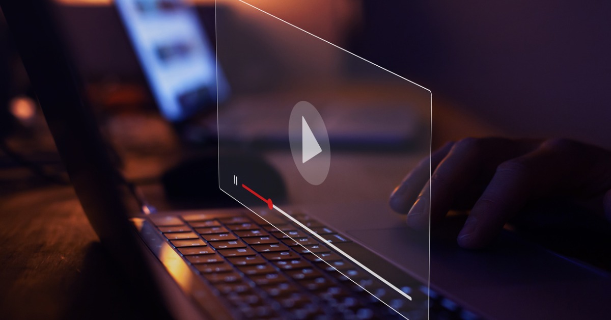 main travaillant sur un pc portable dans l'obscurité avec une fenêtre ouverte sur une page contenant le logo Youtube 