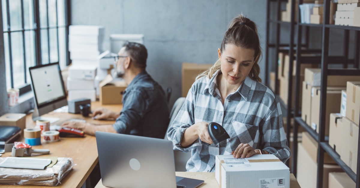 un homme devant un ordinateur et une femme scannant un carton dans un entrepôt 