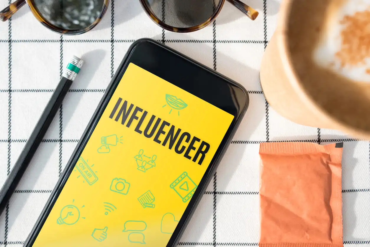 Función Influencer, vista desde arriba en la pantalla del móvil con taza de café, gafas de sol, lápiz de estilo de vida, mantel blanco.blogger