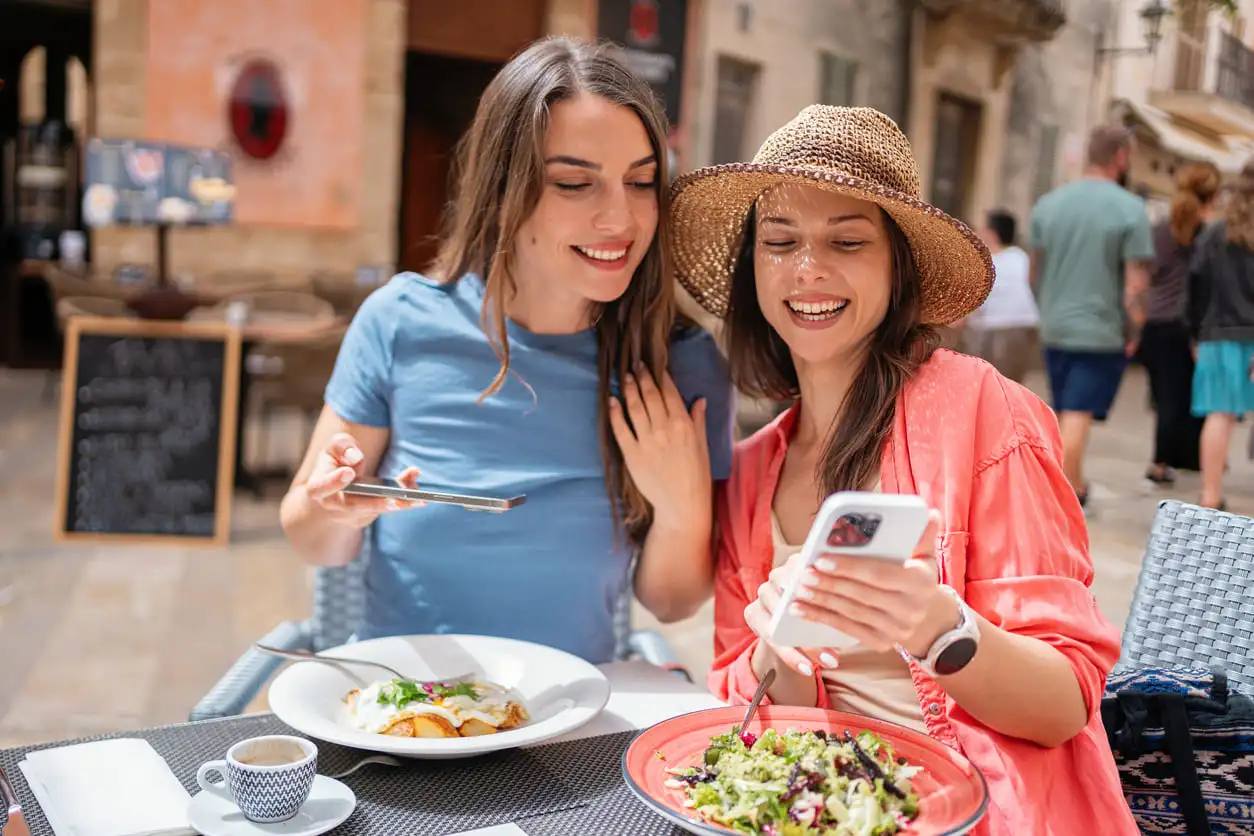 Dos amigos comparten un momento y fotografían sus comidas en un restaurante con terraza en la ciudad de Alcúdia, Mallorca