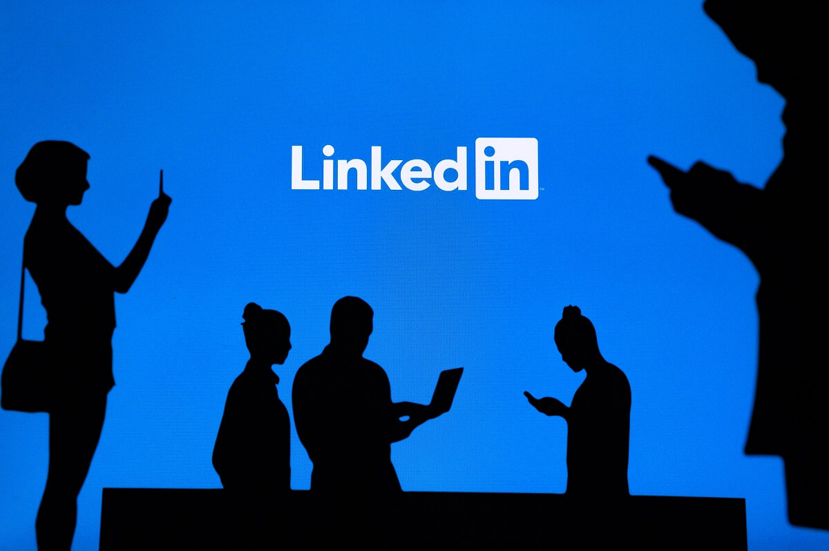 silhouettes noires regardant un téléphone sur un fond bleu avec logo Linkedin au milieu