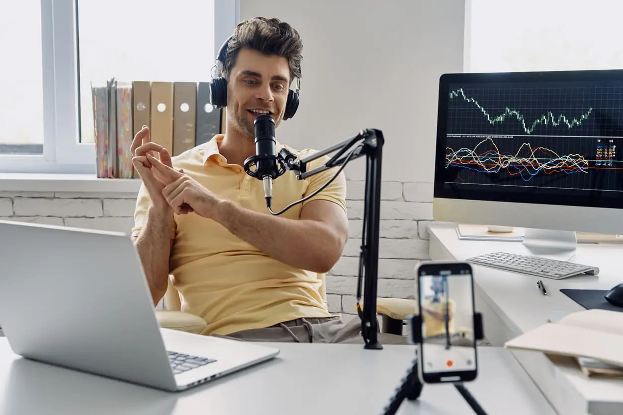 Joven con auriculares que usa un micrófono y gesticula mientras graba su podcast empresarial