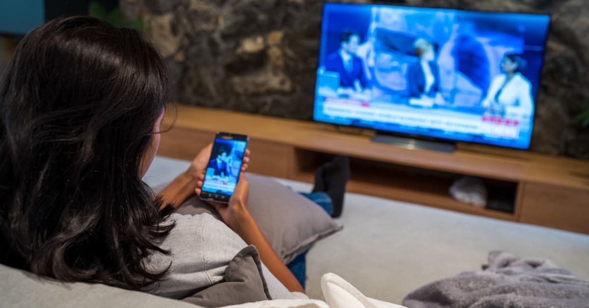 personne assise devant sa télé utilisant son téléphone