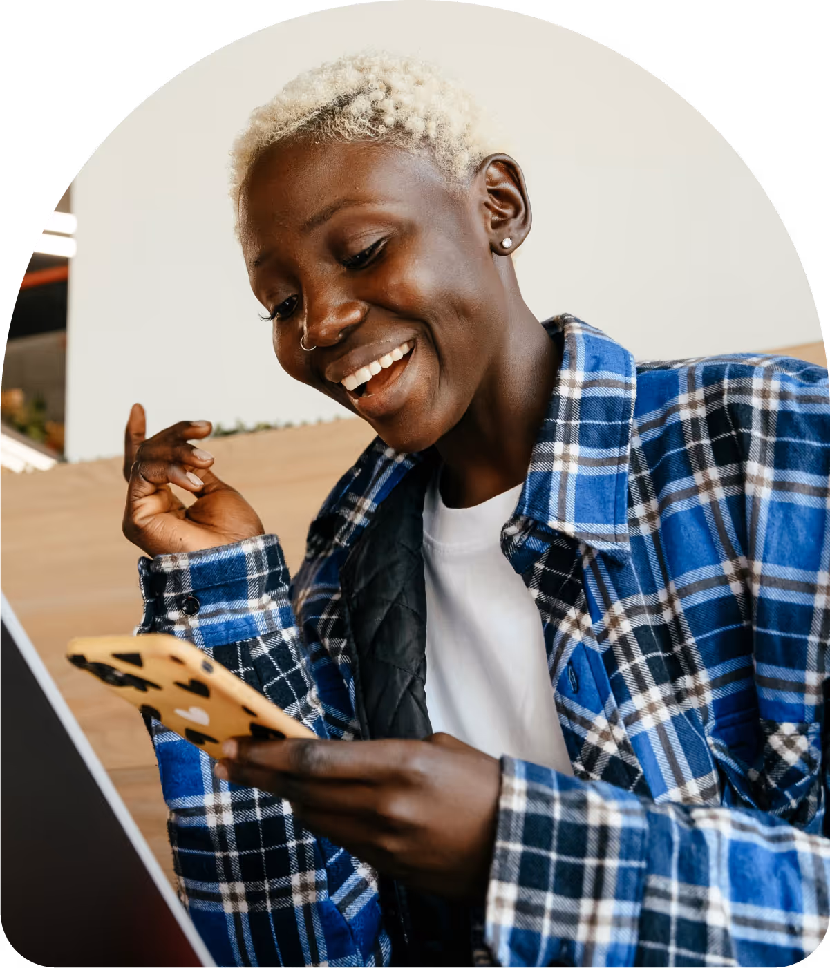 Smiling person with short blonde hair wearing a blue plaid shirt looking at a smartphone.