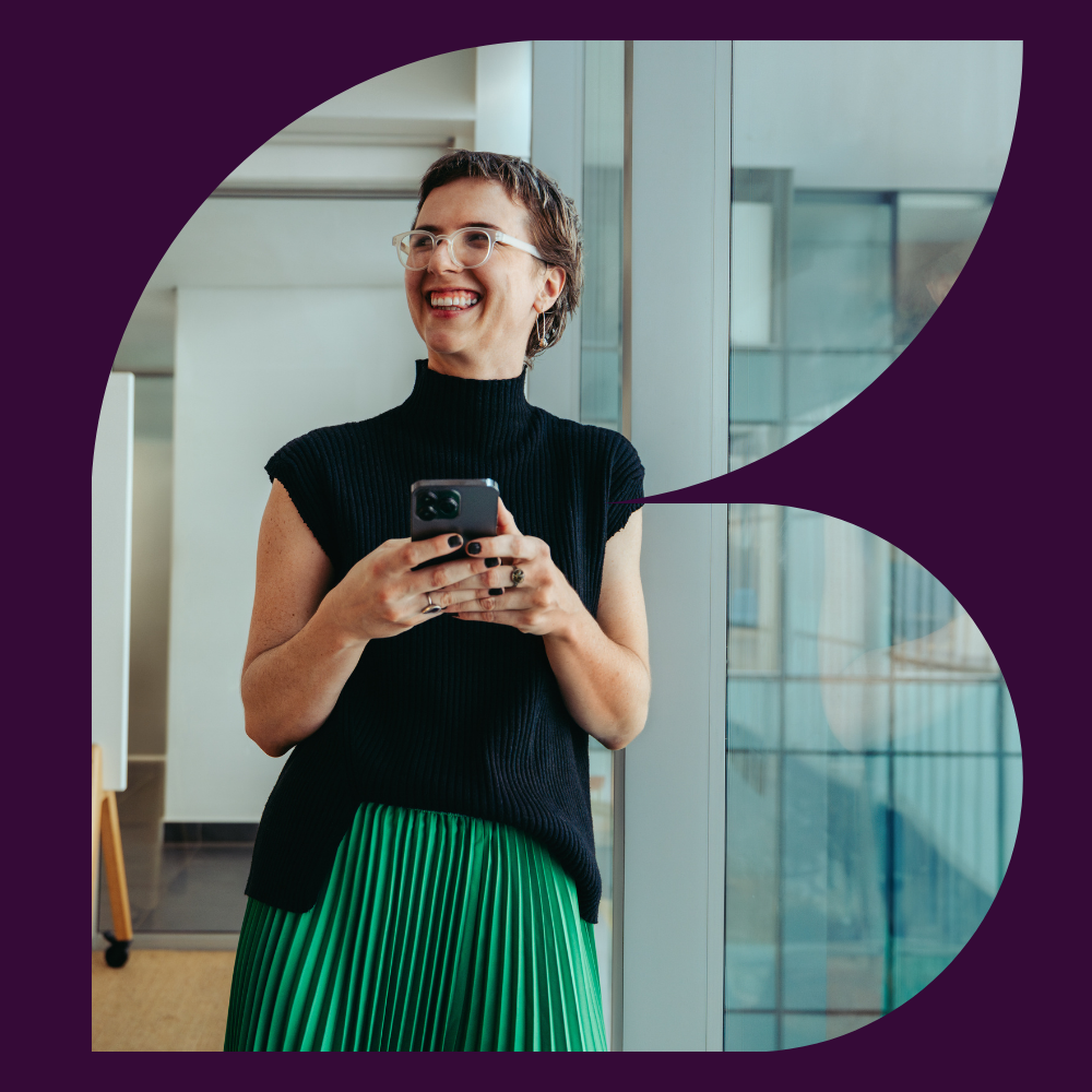 Professional holding a smartphone in a modern office environment.