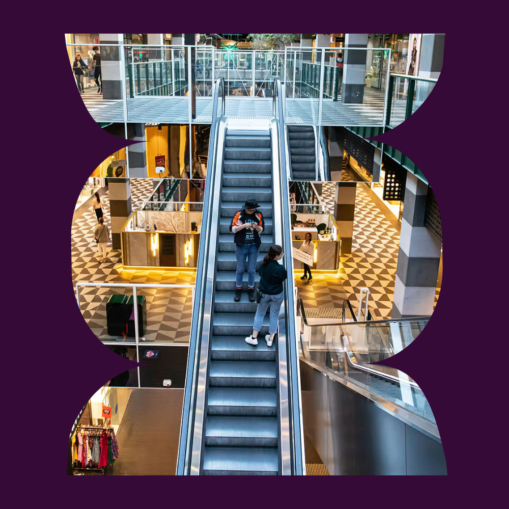 People using an escalator inside a modern shopping centre with multiple retail levels.