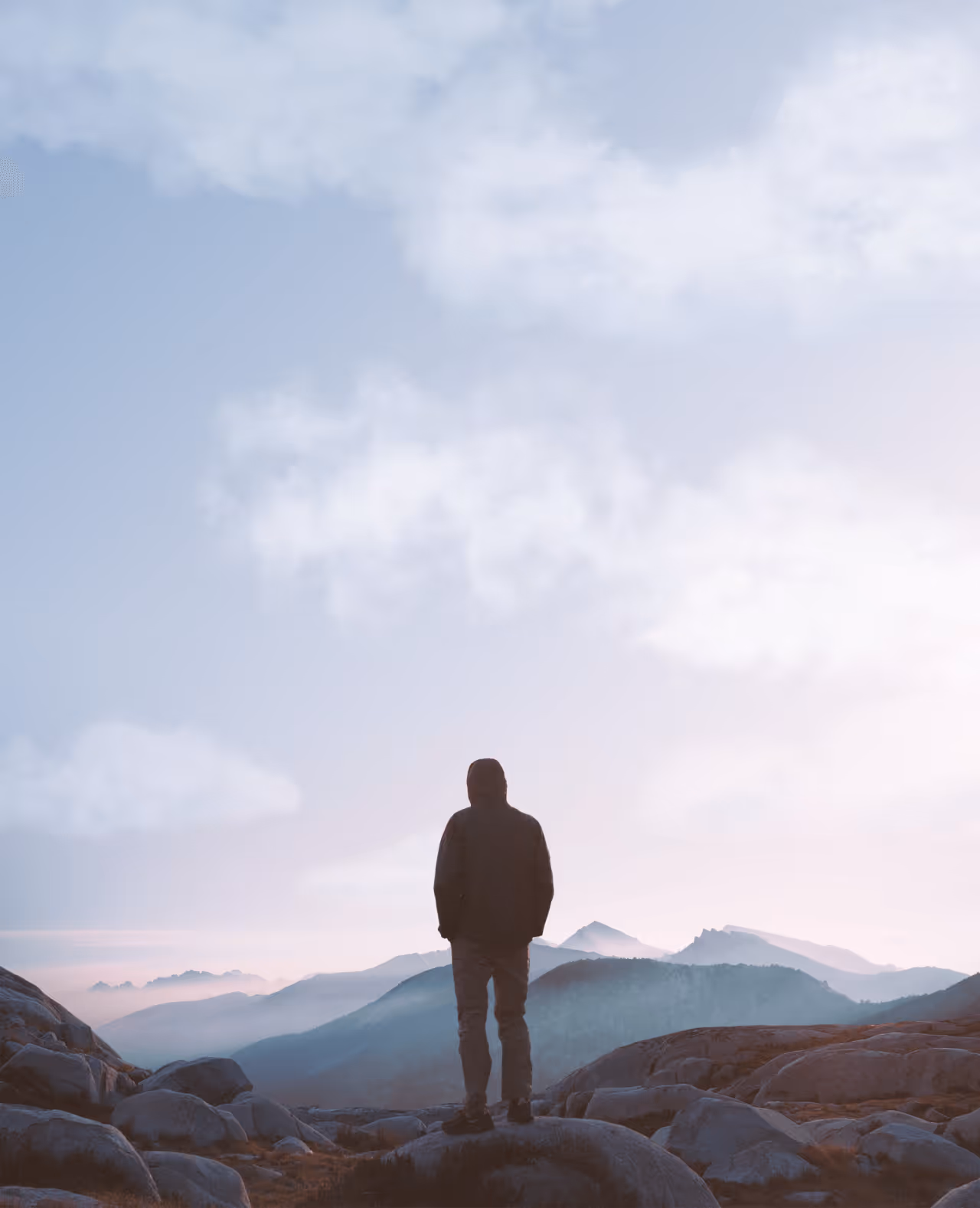 Person in a hooded jacket standing on rocky terrain overlooking misty mountains under a cloudy sky at sunrise or sunset.